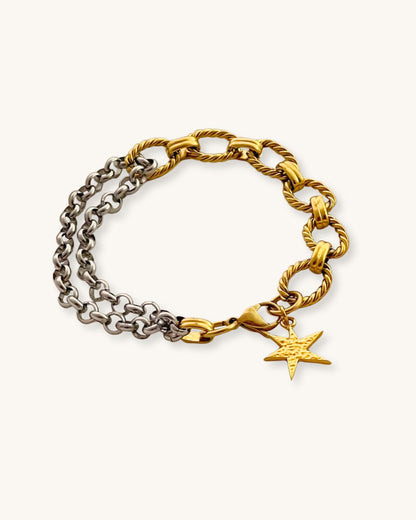 Two chain bracelets, one gold and one silver with a gold charm charm on a light background