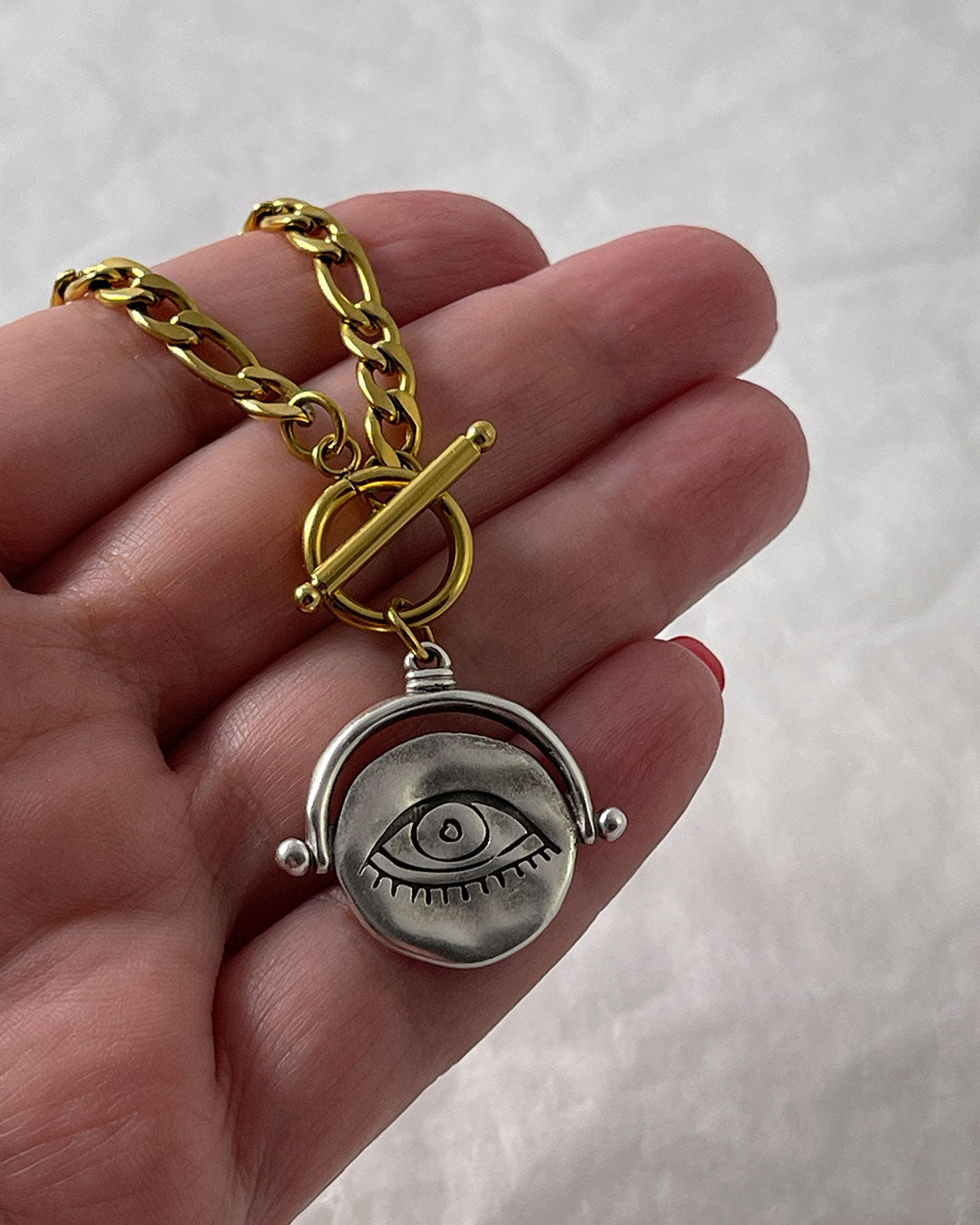Gold figaro chain necklace with a silver eye pendant held in a hand against a white background