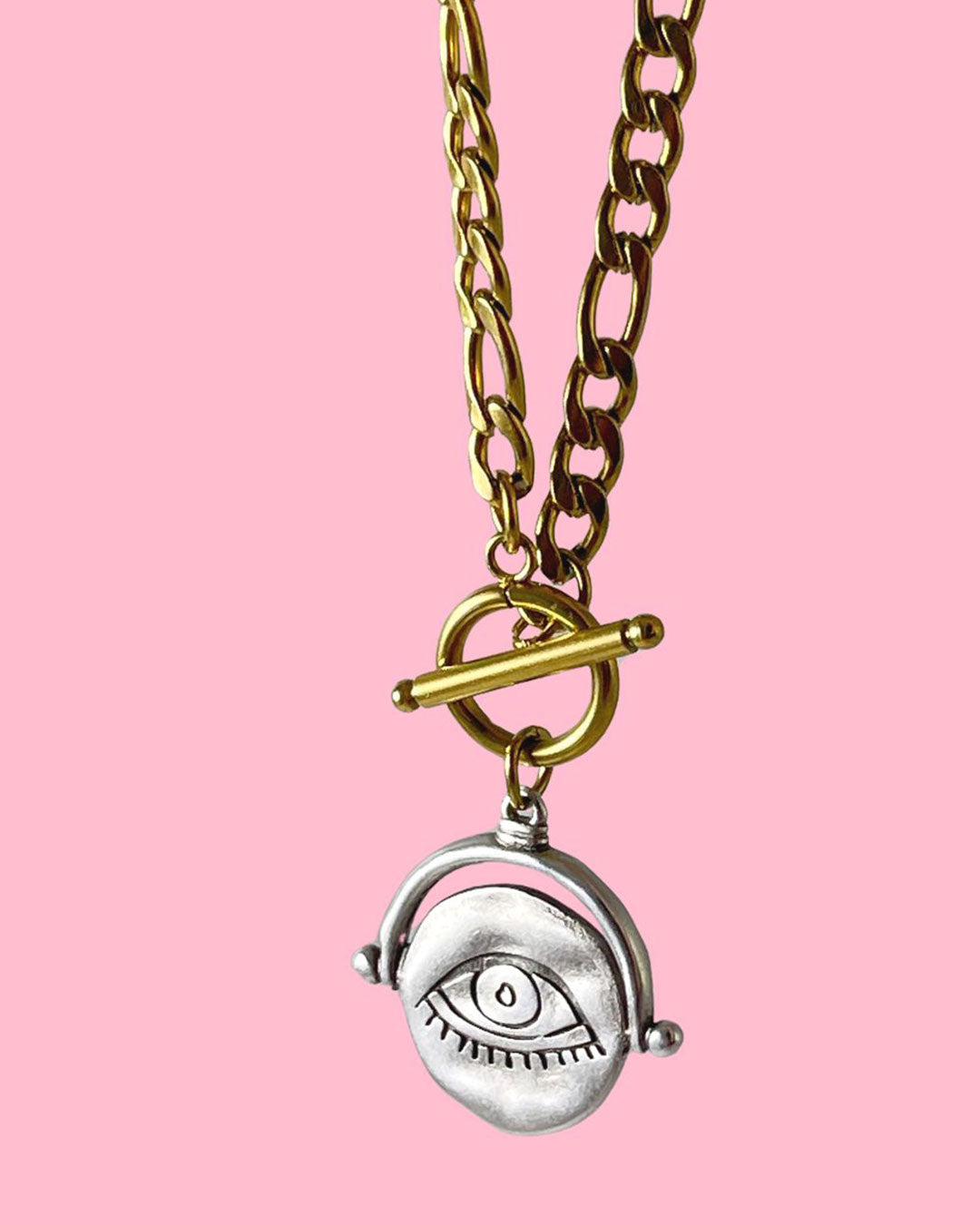 Gold figaro chain necklace with a silver eye pendant on a pink background