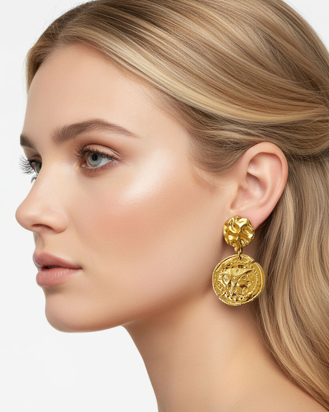 Model wearing gold earrings featuring a raised design of Athena's goddess face accents on a coin.