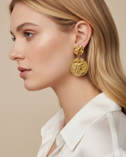 Model wearing gold earrings featuring a raised design of Athena's goddess face accents on a coin.