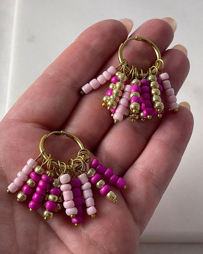 A pair of boho beaded hoop earrings in pink, fuchsia, and gold colors with stainless steel hoops finished in 18K gold
