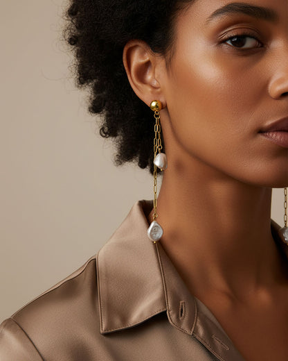 Model wearing a pair of stud earrings featuring two paperclip chains with shell pearl pendants