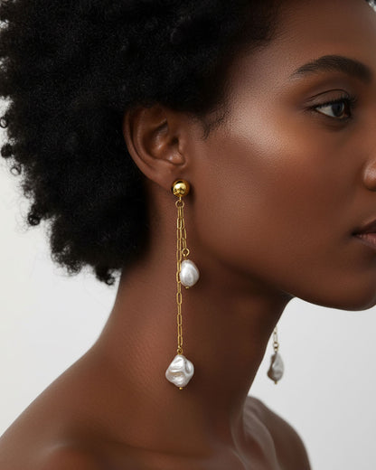 Model wearing a pair of stud earrings featuring two paperclip chains with shell pearl pendants