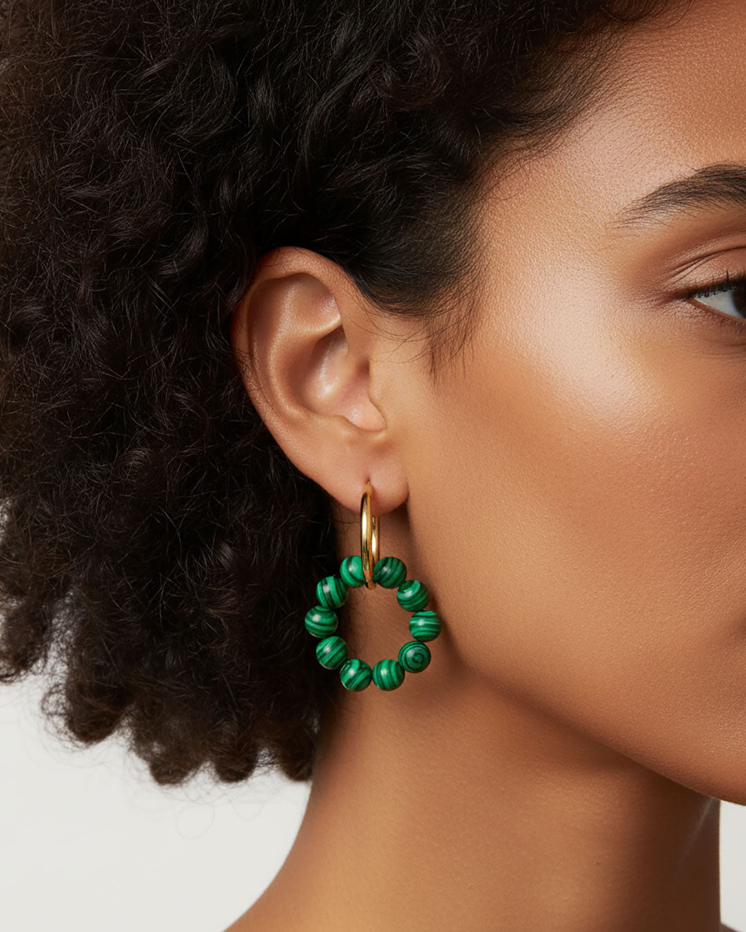 Model wearing gold hoop earrings with malachite green beads