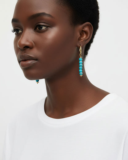 Model wearing a pair of gold hoop earrings with turquoise bead drops