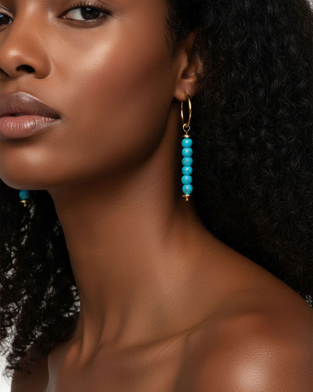Model wearing a pair of gold hoop earrings with turquoise bead drops