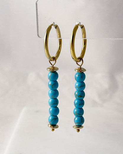The Turquoise Gem Hoop Earrings, a pair of gold hoop earrings featuring turquoise howlite stones.