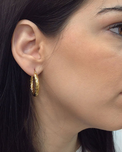 Model wearing a pair of 30mm twisted gold hoop earrings
