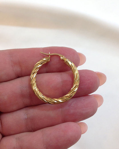 Close up details from 30mm twisted gold hoop earrings on fingers