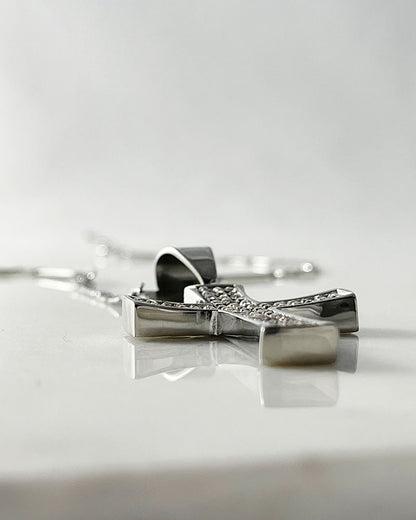 A silver chain necklace with a silver cross pendant. The cross is encrusted with small, clear cubic zirconia stones.