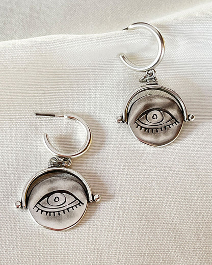 The Evil Eye Bohemian Earrings, a pair of silver hoop earrings featuring an evil eye round charm.