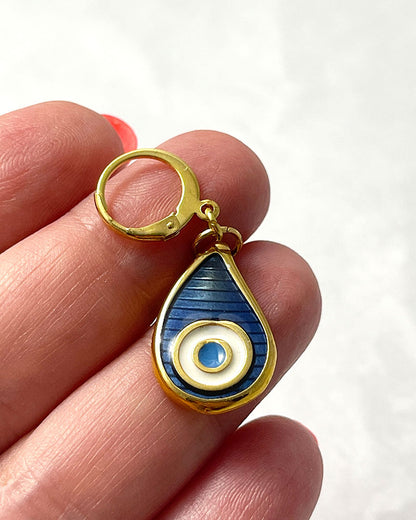 The Eye Drop Earrings, a pair of gold hoop earrings featuring a blue enamel evil eye drop shaped charm.