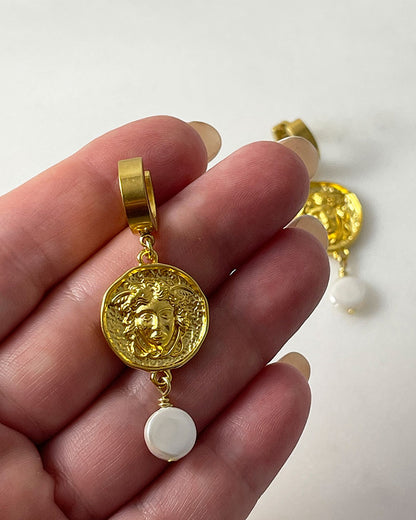 The Medusa Hoop Earrings, a pair of gold hoop earrings adorned with a medusa round charm and a MOP shell pearl.