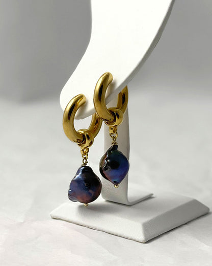 The Black Baroque Pearl Hoops, a pair of gold stainless steel hoop earrings adorned with irregular-shaped black pearls.