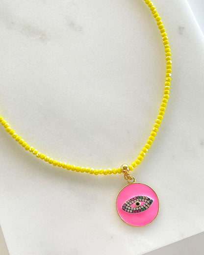 A yellow beaded necklace with a fuchsia round eye pendant.