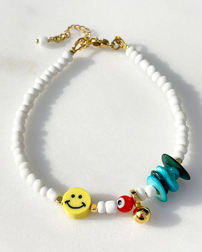 A white beaded anklet adorned with a yellow smiley happy face bead and turquoise shell chips