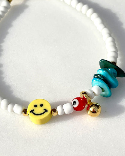 A white beaded anklet adorned with a yellow smiley happy face bead and turquoise shell chips