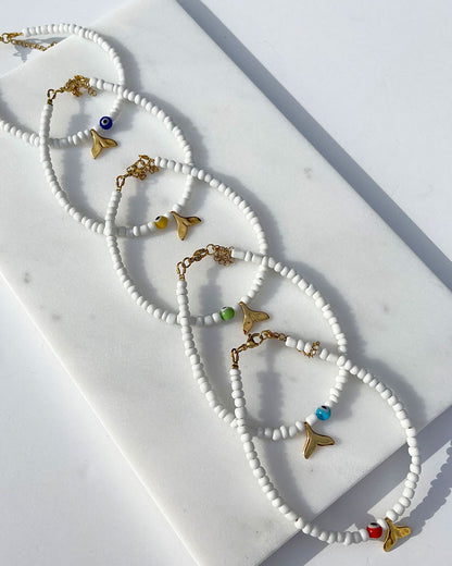 A white glass beaded anklet adorned with a gold tail and a colorful evil eye bead