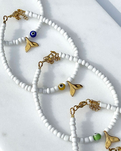A white glass beaded anklet adorned with a gold tail and a colorful evil eye bead