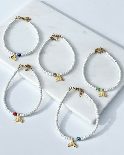 A white glass beaded anklet adorned with a gold tail and a colorful evil eye bead