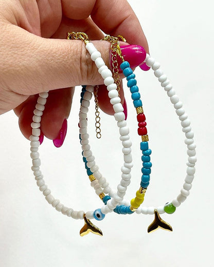A white glass beaded anklet adorned with a gold tail and a colorful evil eye bead