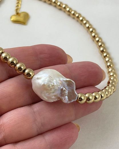 A handmade necklace with gold hematite beads and a large baroque pearl in the middle