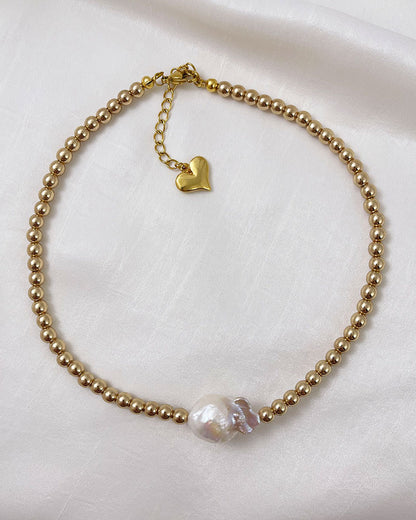 A handmade necklace with gold hematite beads and a large baroque pearl in the middle