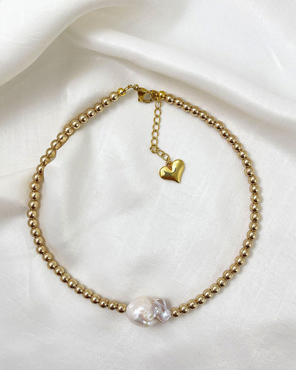 A handmade necklace with gold hematite beads and a large baroque pearl in the middle