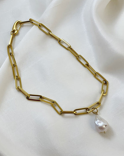 A gold chunky chain necklace with a large baroque pearl in the middle