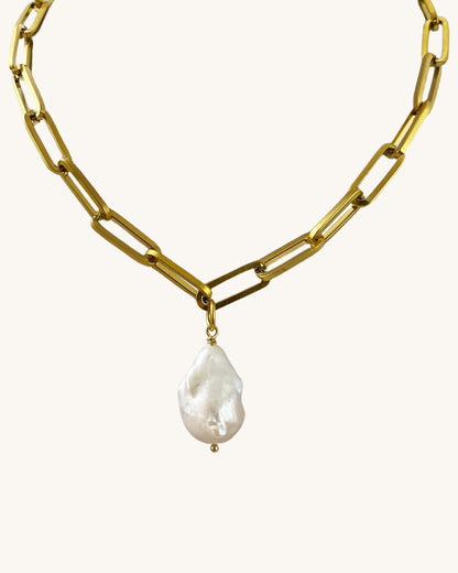 A gold chunky chain necklace with a large baroque pearl in the middle