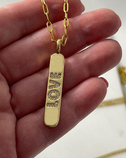 A love engraved tag charm on a dainty paperclip chain in gold
