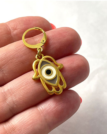 The Hamsa Eye Earrings, a pair of gold hoop earrings featuring a hamsa hand with an eye enamel charm.