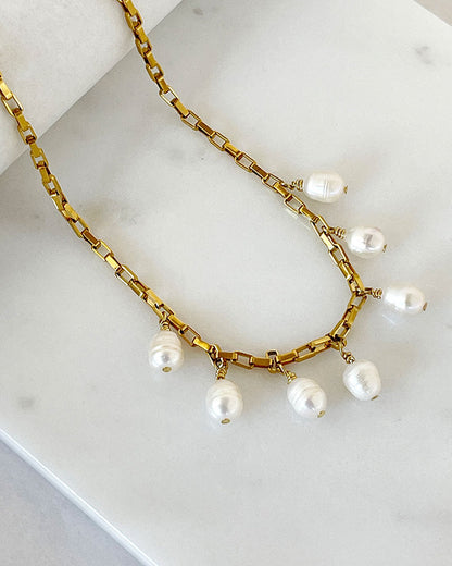 A gold chain necklace with multiple white pearl drops