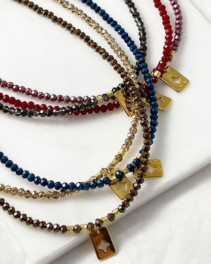 Shiny glass beaded necklaces in different colors with a gold star tag pendant.