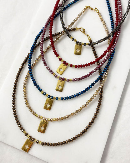 Shiny glass beaded necklaces in different colors with a gold star tag pendant.